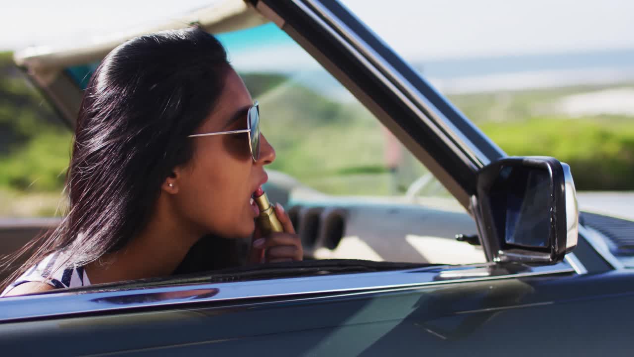 African american woman applying lipstick while looking in the mirror of convertible car
