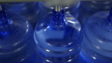 a close-up view of an automated machine filling large blue water containers in a water bottling facility