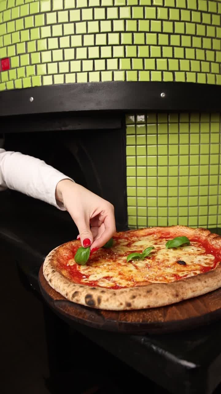 Mano che adagia foglie di basilico fresche su una pizza Margherita calda