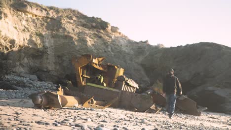 Young-man-walking-through-intriguing-shipwreck-remains-on-the-beach