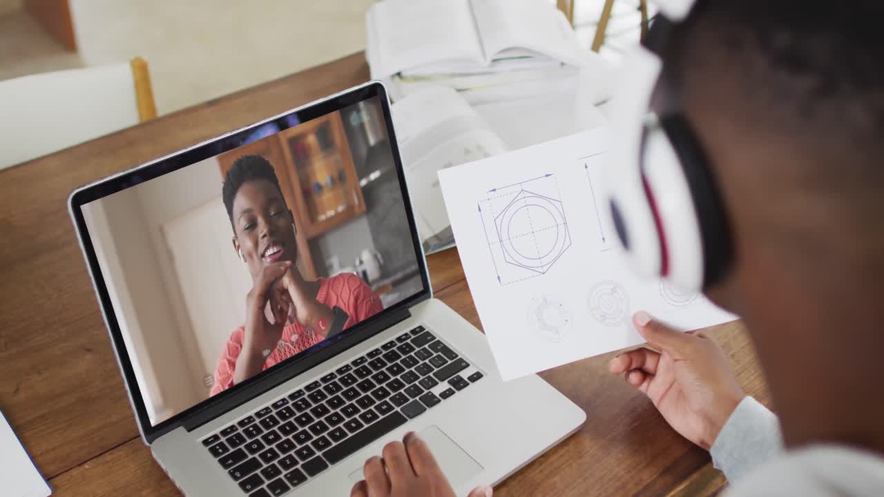 estudiante universitario afroamericano que sostiene notas mientras hace una videollamada en una computadora portátil en casa