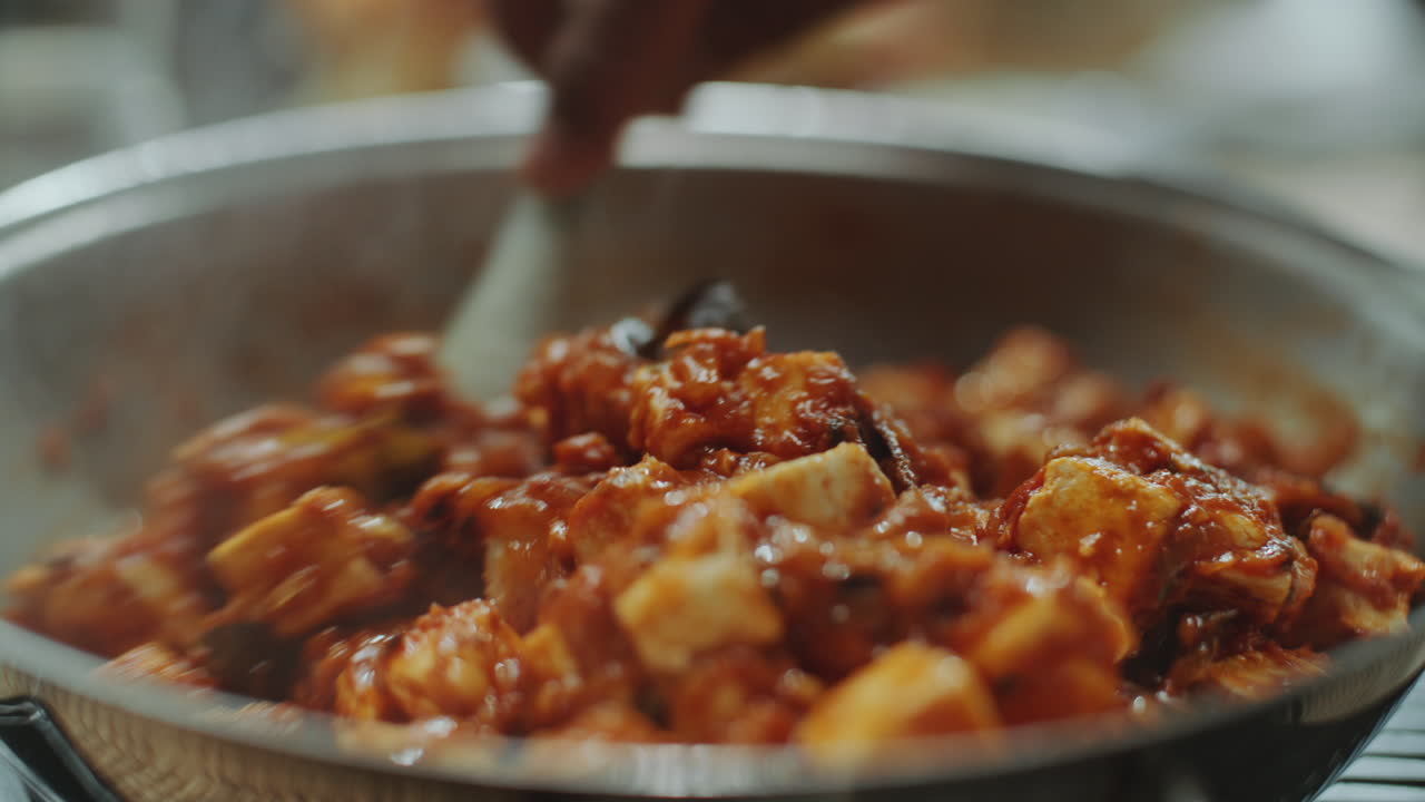 mano del chef agitando un plato de tofu picante con espátula en una sartén grande