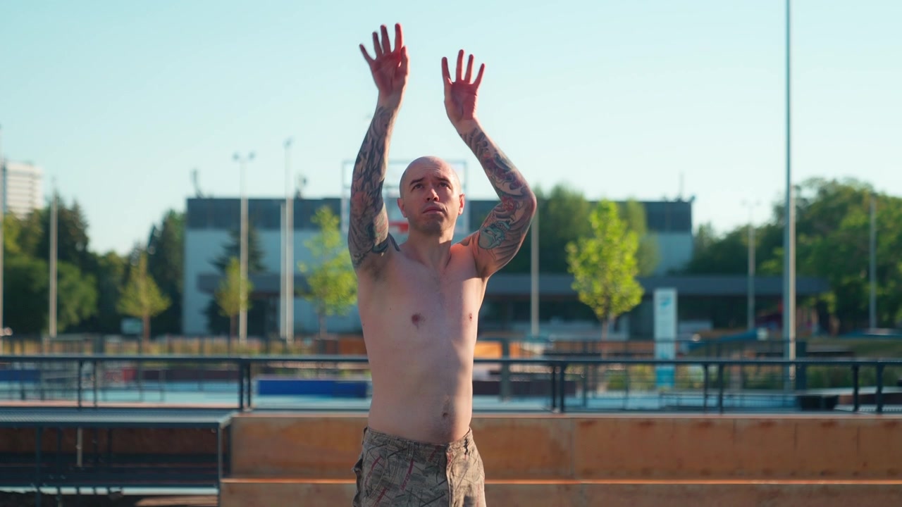 Uomo calvo e tatuato lancia e afferra un pallone da basket su un campo all'aperto