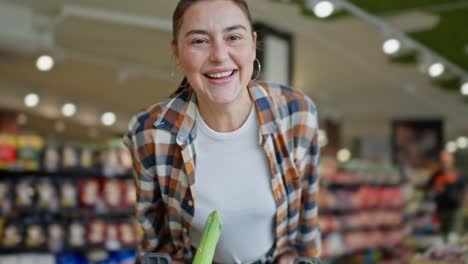 Happy-brunette-woman-in-a-plaid-shirt-leans-on-a-cart-and-spins-during-her-fun-shopping-in-a-supermarket