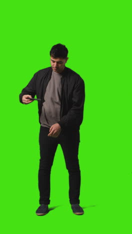 vertical video full length shot of young woman holding blue screen mobile phone to camera standing against green screen