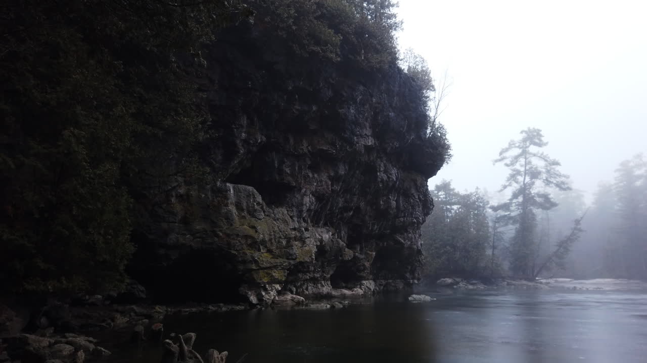 A limestone cliff towers over a rugged winter landscape and calm, icy water, low angle wide shot with tilt down to water's edge