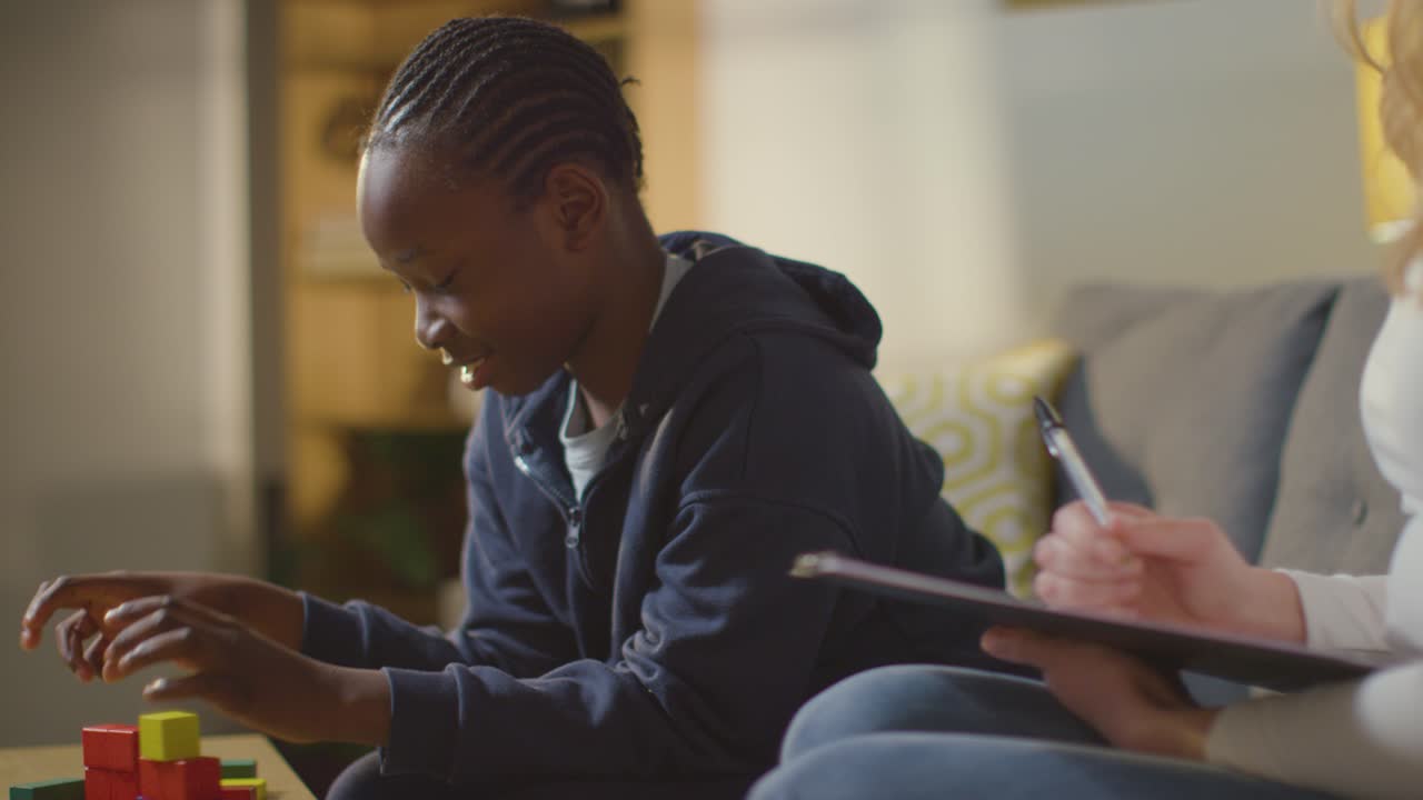 Boy On ASD Spectrum Being Helped Or Assessed By Female Teacher Or Educational Psychologist At Home 5