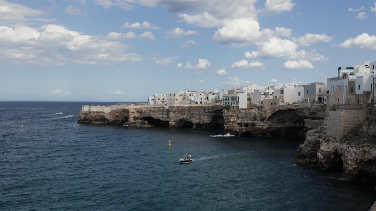 Tur perahu wisata di dekat pantai berbatu dengan bangunan putih di Polignano, Puglia, Italia.
