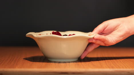 person's hand served the bowl of mixed berries with oats on a wooden table