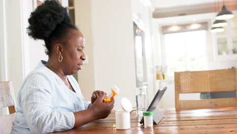 African-american-senior-woman-having-video-call-and-holding-medicines-in-sunny-room,-slow-motion