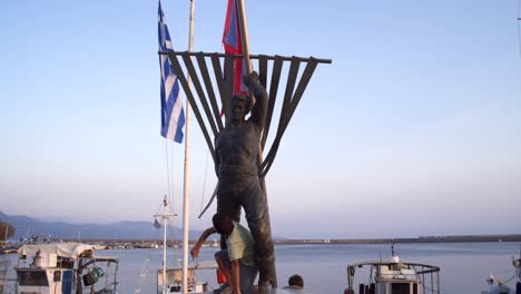 two caucasian brothers standing under a bronze statue of sailor, located at kalamata's small port peloponnese, greece