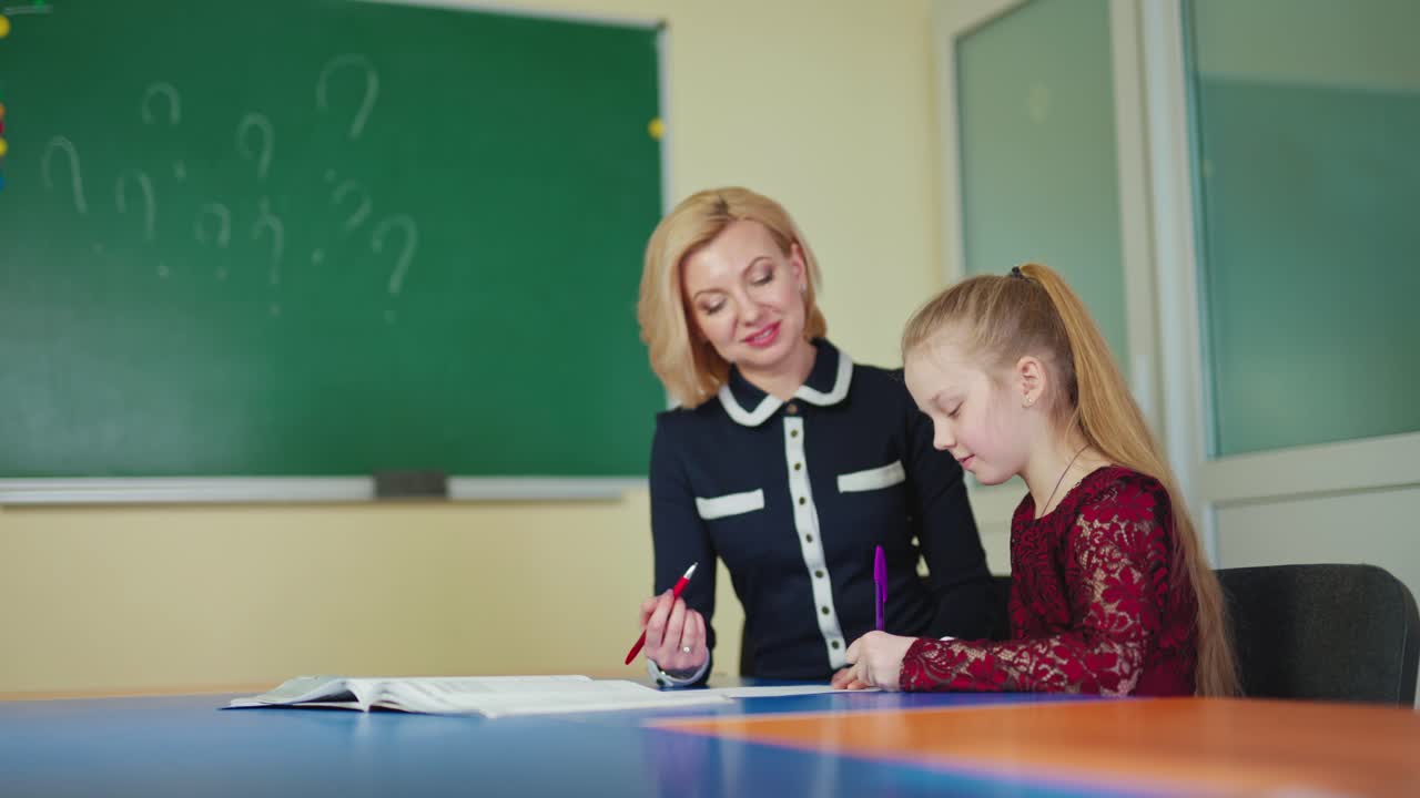 Female tutor with a little girl. Schoolgirl together with a beautiful teacher smiling while studying on the classroom background. Education concept.