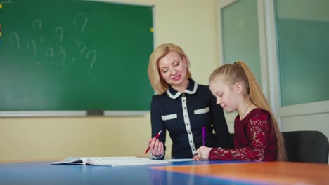 female tutor with a little girl. schoolgirl together with a beautiful teacher smiling while studying on the classroom background. education concept.