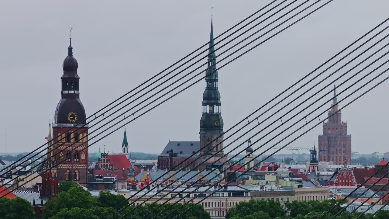 Overcast drone flight through bridge cables shows rainy Riga skyline with tower