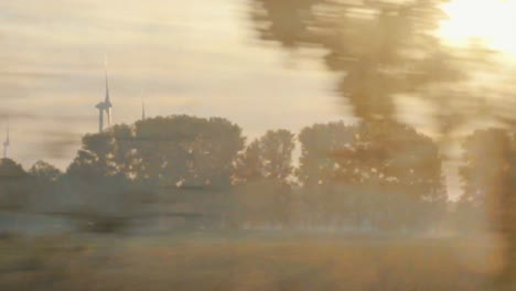 windmills on countryside field during beautiful sunset seen from a moving train