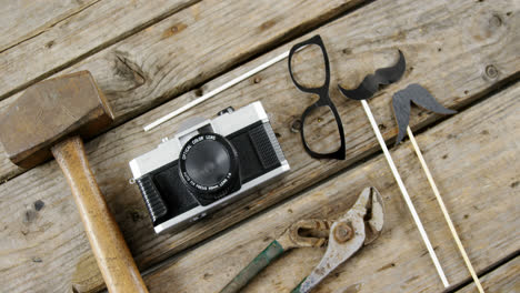 Work-tool,-Vintage-camera,-spectacles-and-fake-mustache-arranged-on-wooden-plank