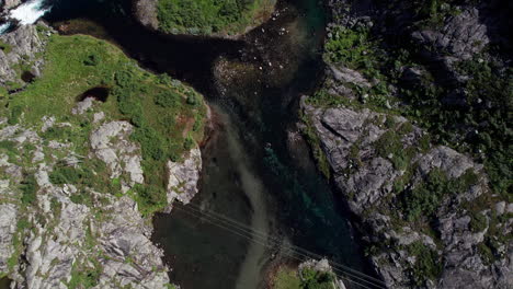 Bird‘s-eye-view-of-a-small,-shallow-river-as-it-flows-through-a-rocky,-mossy-landscape