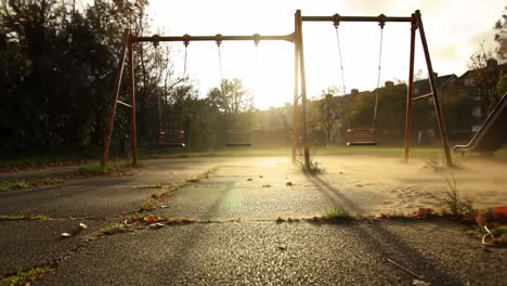 A serene playground scene captured during sunset, showcasing two empty swings gently swaying in the breeze amidst a tranquil, leaf-strewn environment