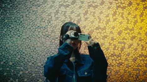 woman holding vintage retro camera while standing in front of mosaic glass portrait of creative teen