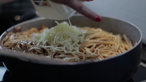 picar queso parmesano sobre espaguetis en una sartén