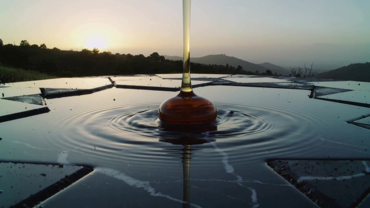 Dropping amber viscous stream forming bulb and spreading ripples on star tile at sunset