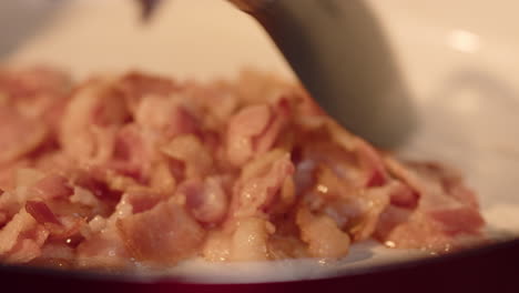 extremo de cerca en la cuchara agitando el tocino mientras se convierte en sartén caliente