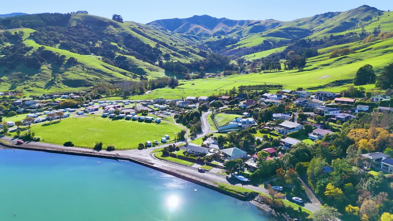 Aerial footage captures Akaroa's vibrant landscape with lush hills, serene waters, and charming town under bright daylight