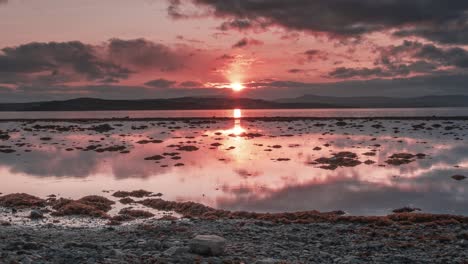 puesta de sol roja de fuego y nubes oscuras reflejadas en las aguas tranquilas del fiordo