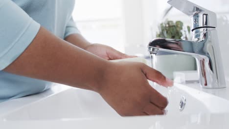 Midsection-of-african-american-woman-washing-hands-with-soap-at-bathroom-sink,-slow-motion