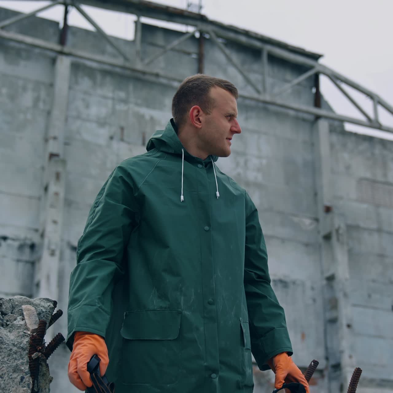 Survivor breathing deeply in destructed place. Man in protective suit holding safety gas mask in hands in enjoys fresh air on the background of ruined building