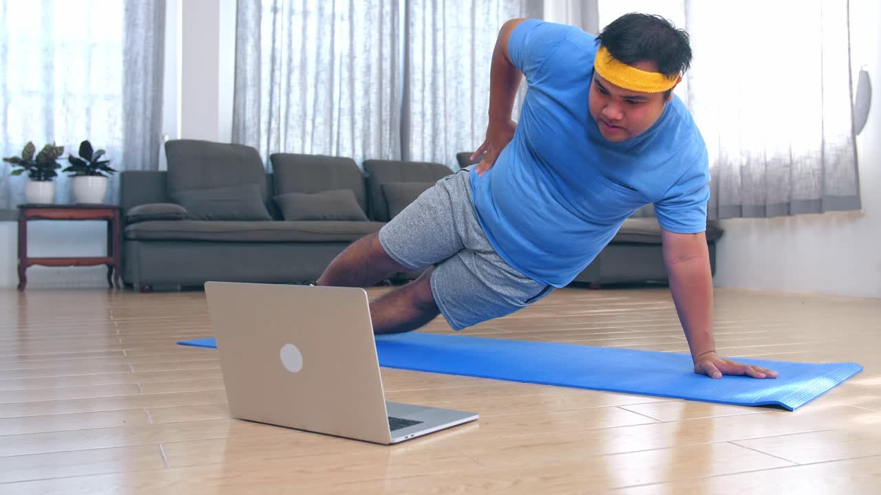 Fat Man Doing Exercises At Home While Watching Online Tutorial On Laptop