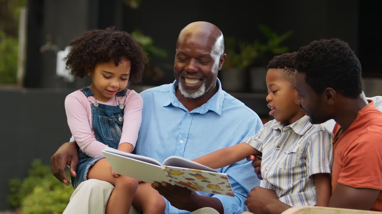 Smilende familie i flere generationer læser bog i haven sammen.