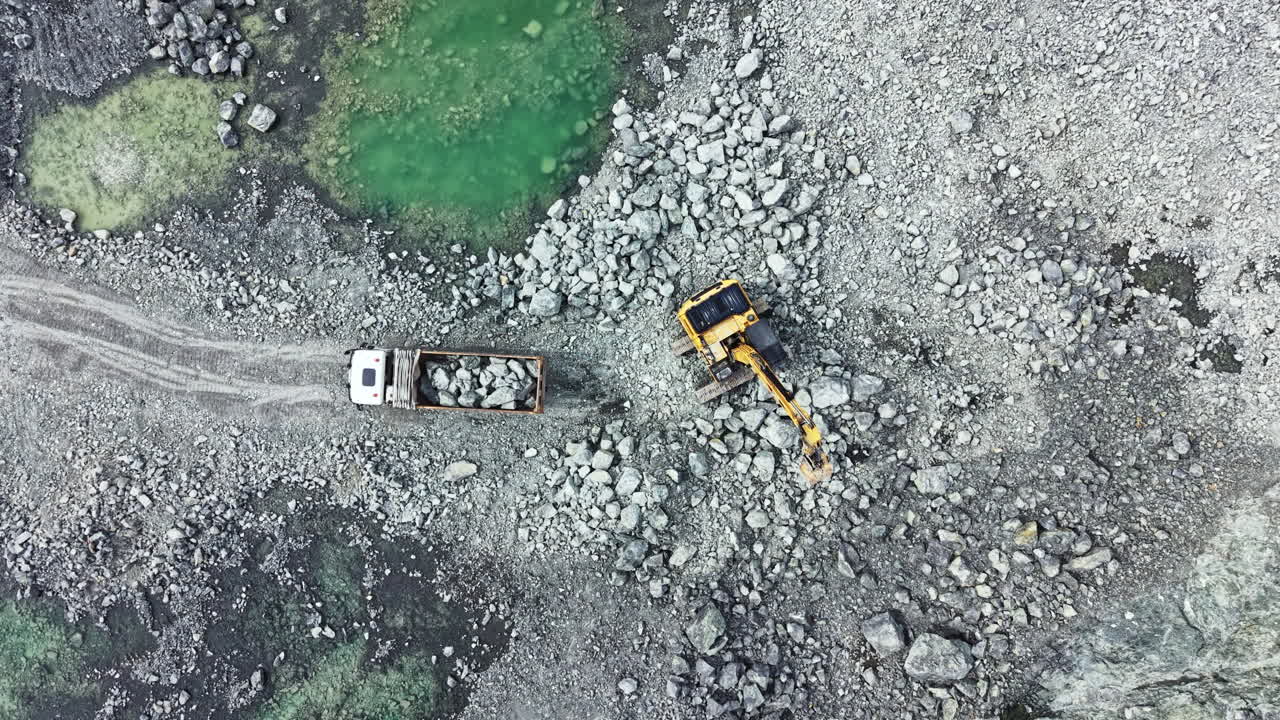 Granite quarry located in a rocky area with machinery working to extract stone and load it into a truck during the daytime