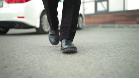 close-up leg view of individual walking outdoors, with background featuring parked white car and building, footsteps in urban environment, highlighting casual walk near vehicle