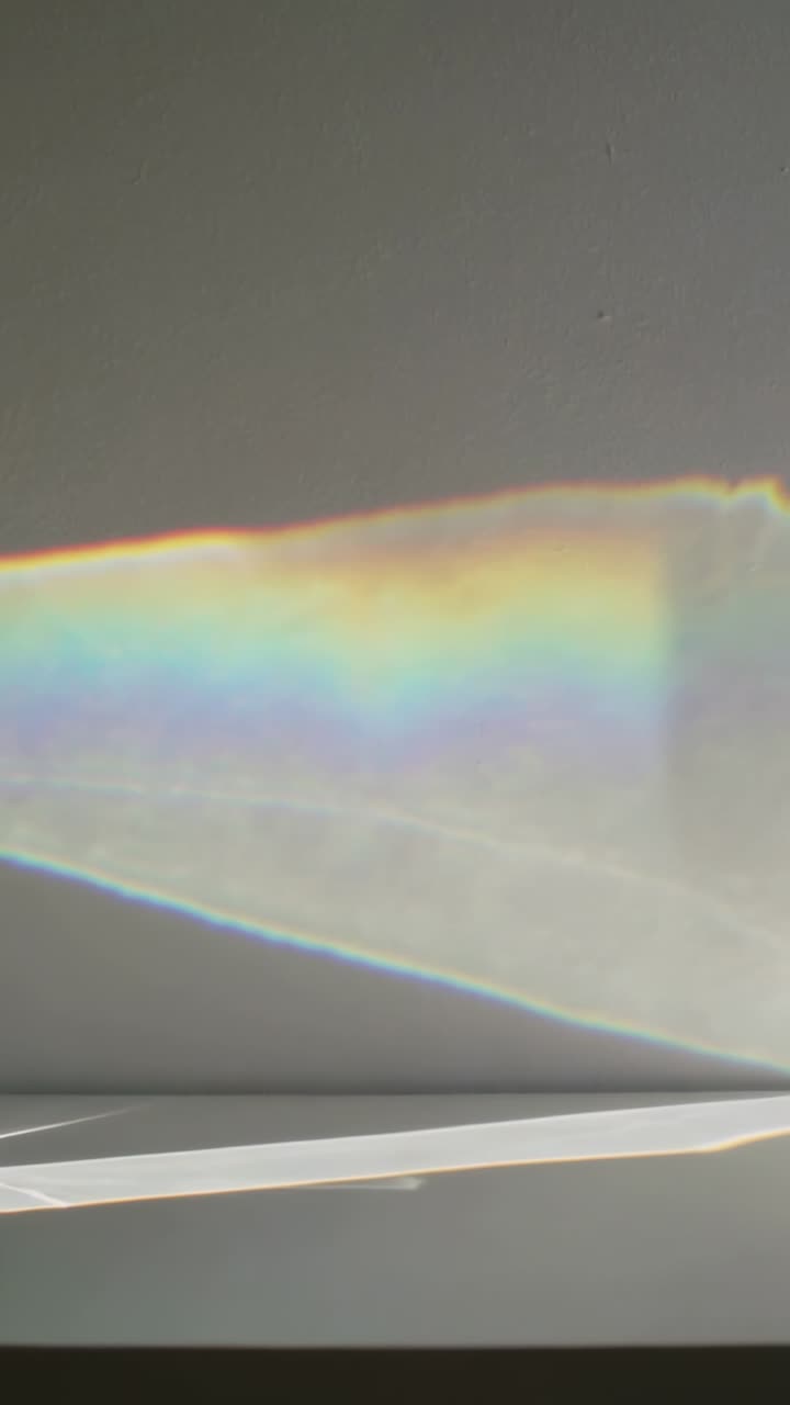 Vertical video: Shifting rainbow band moving across gray wall above table from sun hitting prism