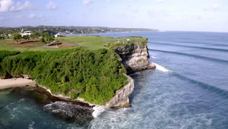 new kuta golf course at dreamland beach in bali indonesia near ocean cliff with waves hitting rocky shore, aerial pedestal rising shot