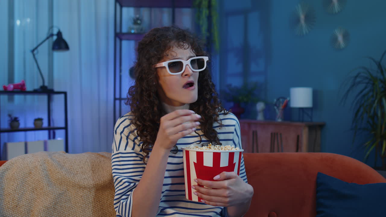 mujer sentada en el sofá comiendo palomitas de maíz y viendo interesantes series de televisión, juegos deportivos en línea en casa