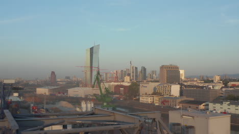 View-on-Frankfurt-am-Main,-Germany-Skyline-from-Port-Area-with-Cranes-in-foreground,-Slow-Aerial-forward-high-angle