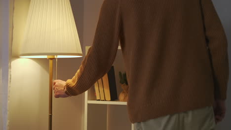 man is switching on light of floor lamp in living room at evening closeup view of hand pulling rope interior of modern apartment