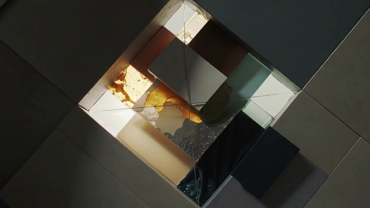 Kamera bergerak mundur menunjukkan panel-panel yang ditumpuk di atas meja untuk menampilkan persegi panjang putih, gel kuning, noda hijau.