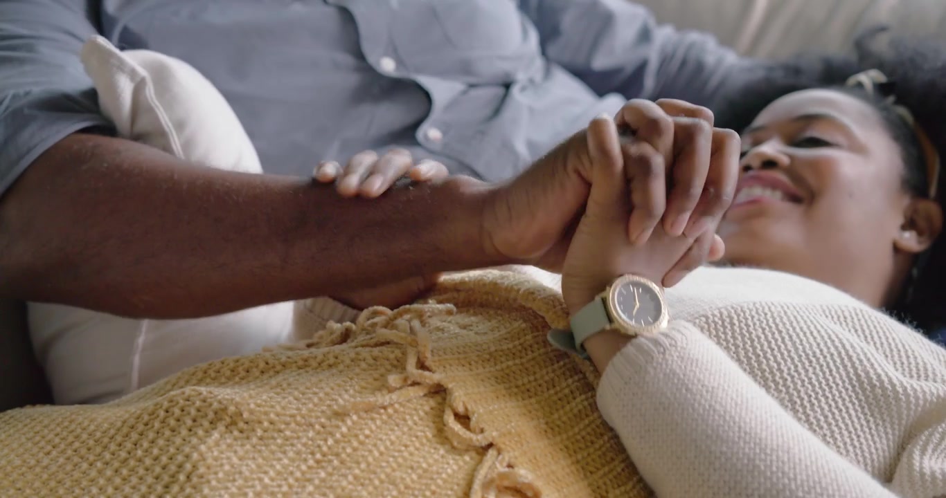 Coppia sdraiata sul divano mentre la donna parla, l'uomo che si allunga, le tiene la mano, confortandola, con un orologio verde.