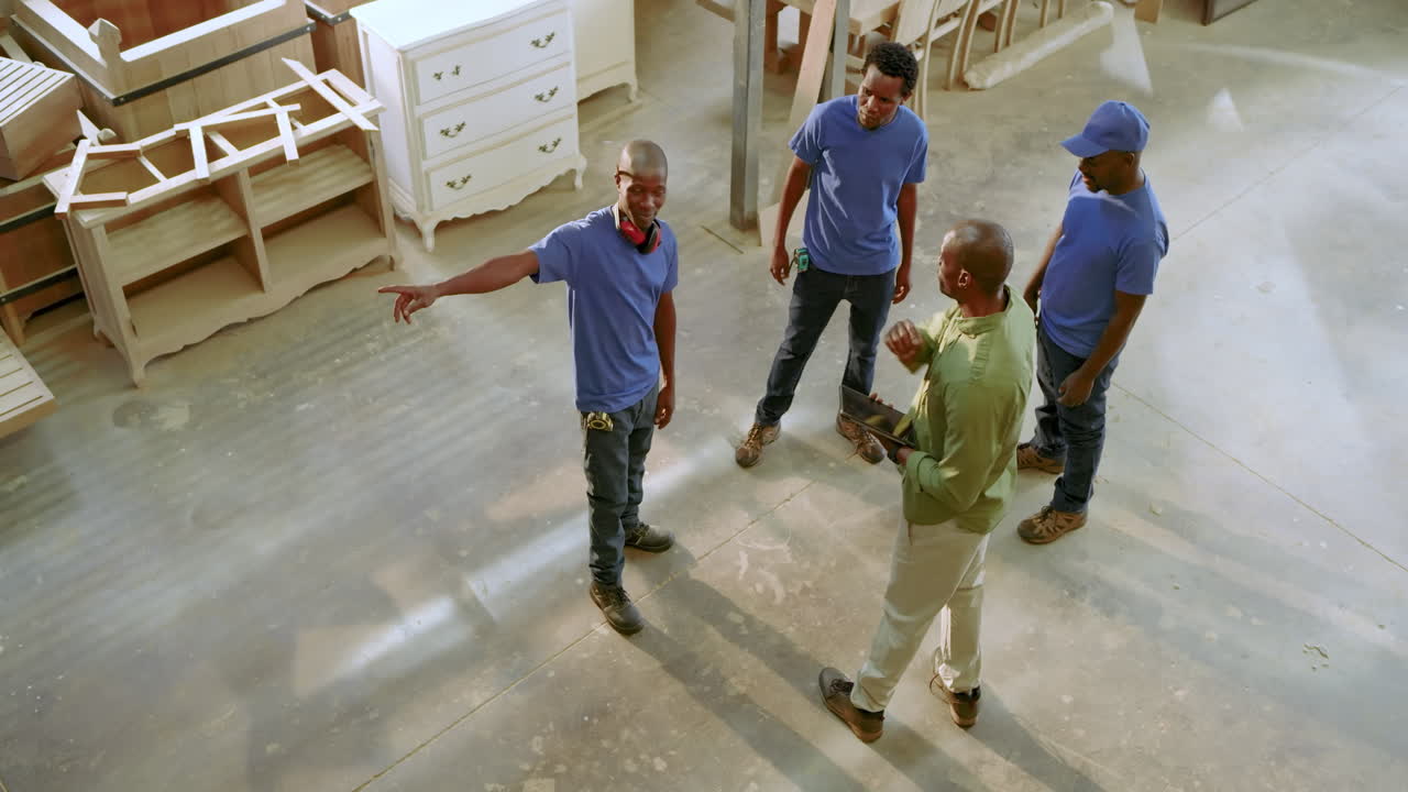 African American man leading workers as unfolding clipboard plan and assigning tasks in workshop