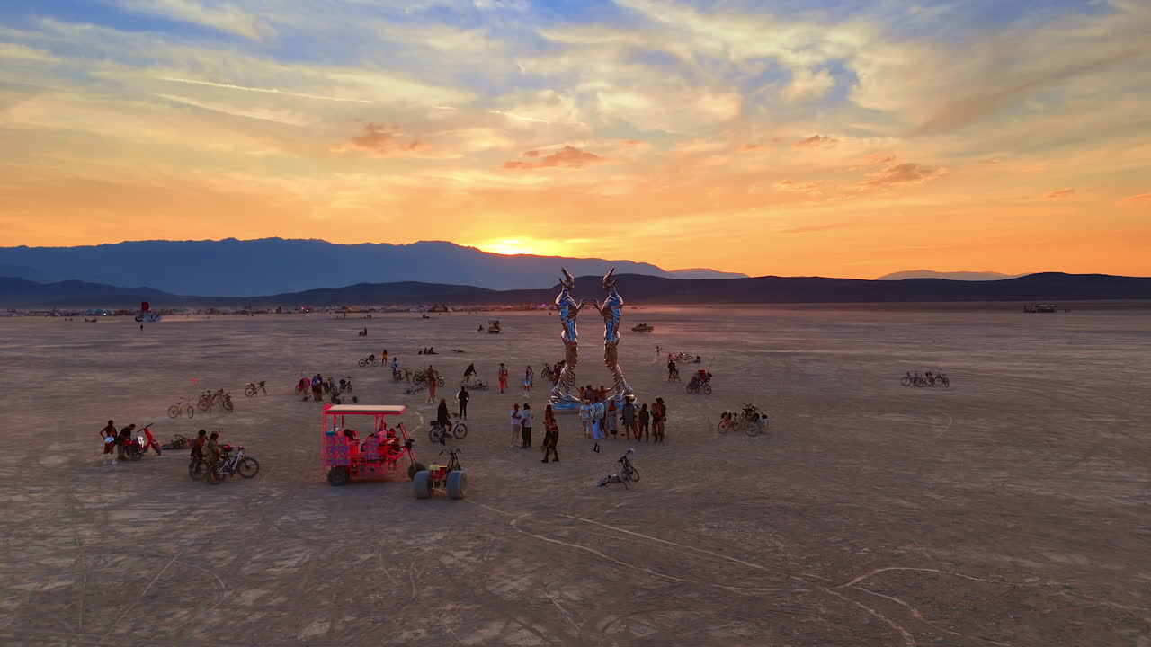Nevada, USA, 14 August 2025: Golden Sunset and Art Installations on the Playa. A golden desert sunset lights up art structures and groups of participants across the wide playa