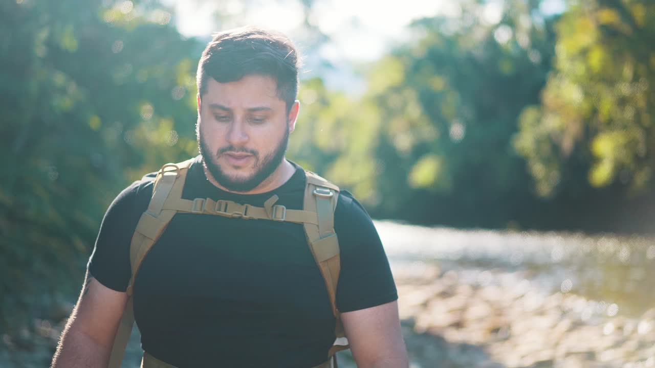 joven excursionista masculino en paseos a lo largo de un río rocoso día caluroso de verano, entrando en la dirección de la cámara cerca de la actividad al aire libre y viajar en la naturaleza