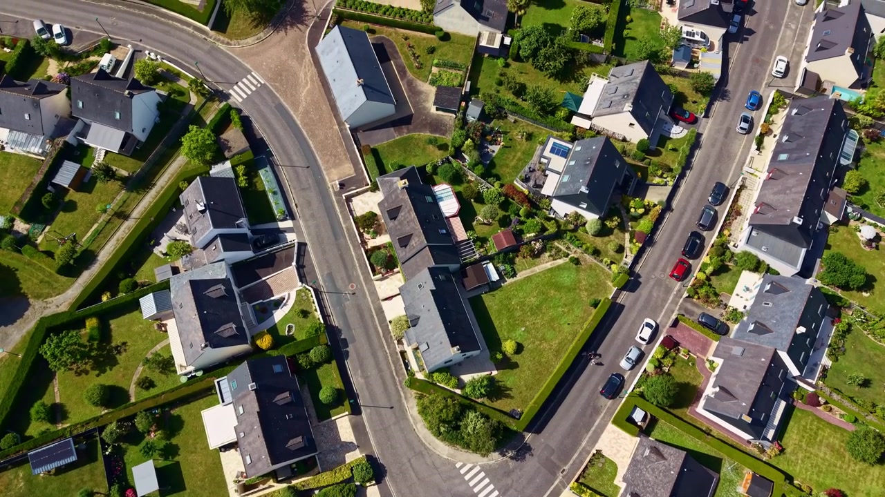 Drone che vola dall'alto sopra un quartiere residenziale con case, giardini, auto parcheggiate e una piscina in una zona suburbana