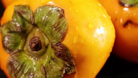 detailed view of a ripe persimmon with water droplets on its surface, highlighting its vibrant color and texture.