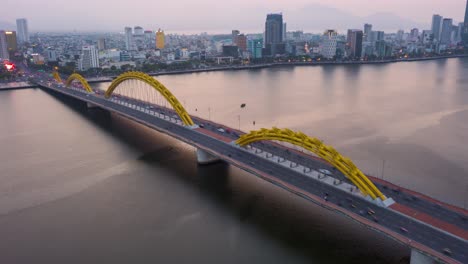 Stunning-colorful-aerial-hyperlapse-of-iconic-landmark-Dragon-Bridge-Cau-Rong,-traffic-and-city-skyline-changing-colors-during-sunset-in-Danang,-Vietnam