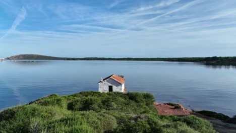 drone rising from behind mountains in menorca spain to show small boat shed in fornells bay with rocky entrance