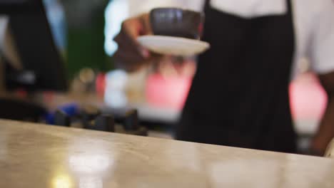 midsection of african american male barista serving coffee in brown coffee cup