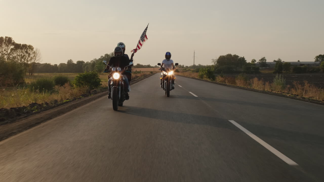 siluetas de ciclistas viajan por la carretera al atardecer con la bandera estadounidense